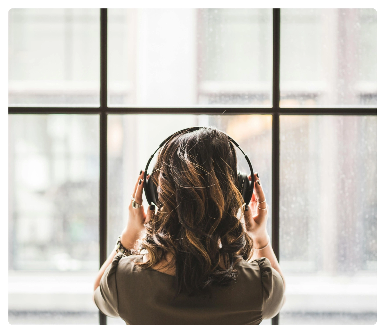 A woman with headphones is looking out the window.