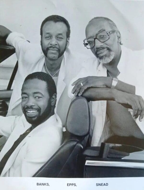 Three men sitting in a car smiling for the camera.